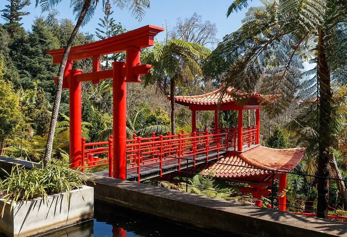 A red bridge and ornamental gateway in Monte Palace’s gardens, beside the paths of a garden walk.