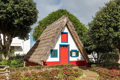 A white, red and blue thatched house in Santana beside the garden paths of a village visit.